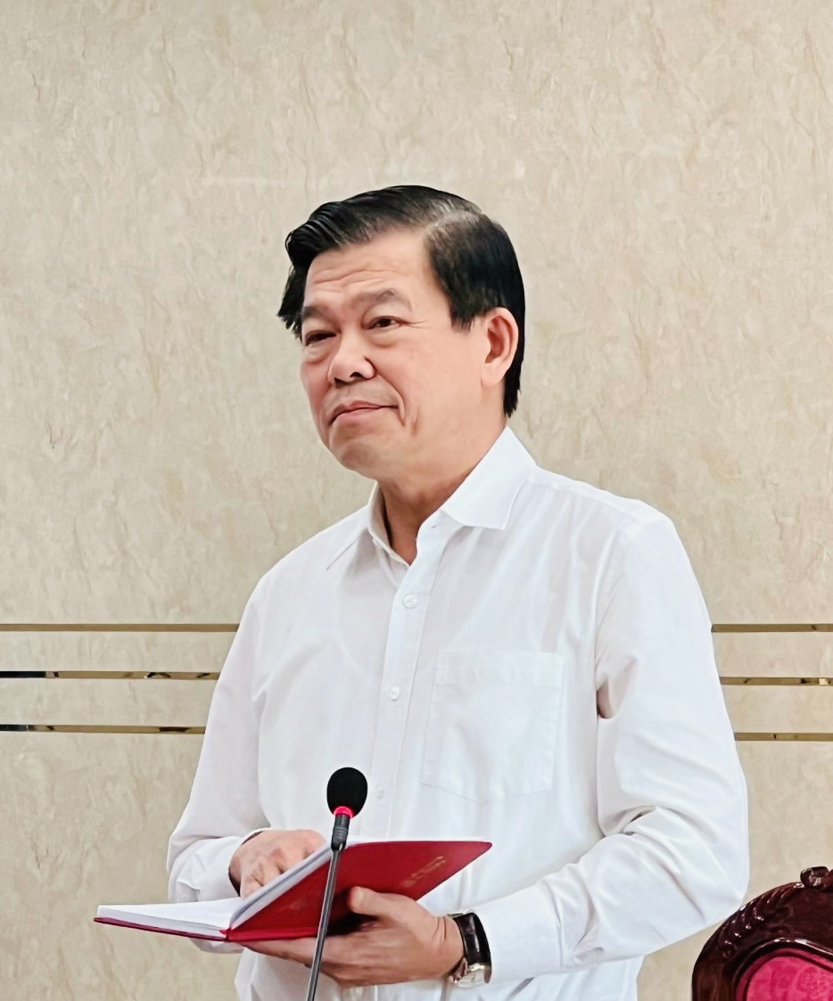 A person in a white shirt holding a red book and a microphoneDescription automatically generated