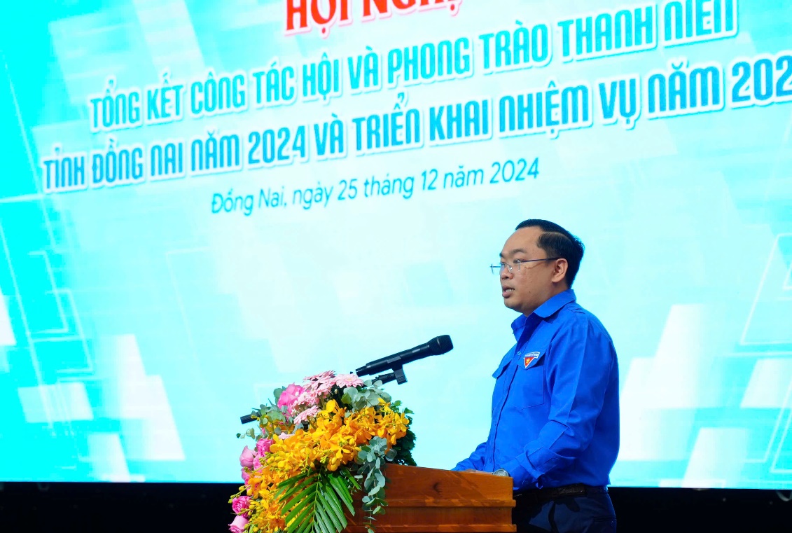 A person standing at a podium with a microphone and flowersDescription automatically generated