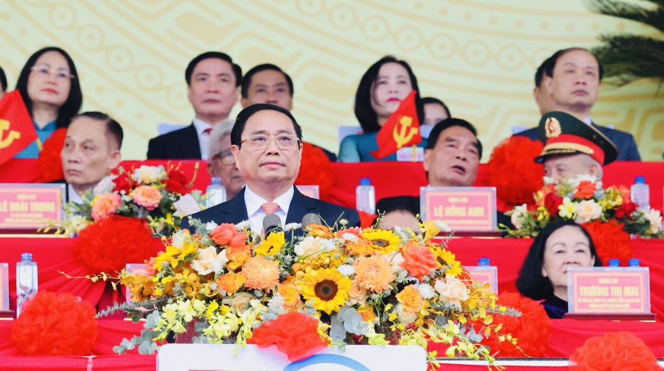 A person in a suit with a microphone and flowers in front of himDescription automatically generated