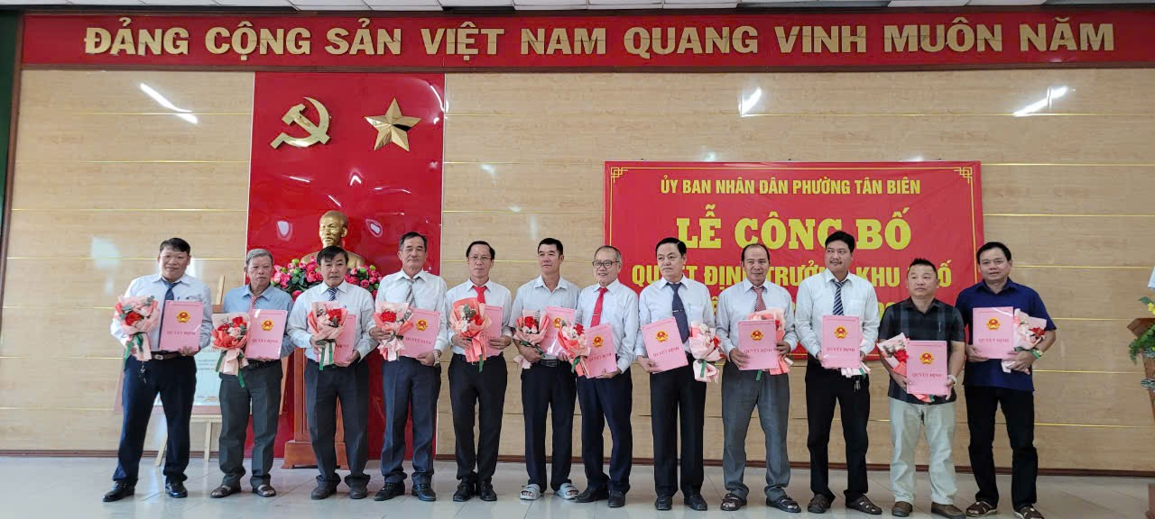 A group of men standing in a row holding flowersDescription automatically generated